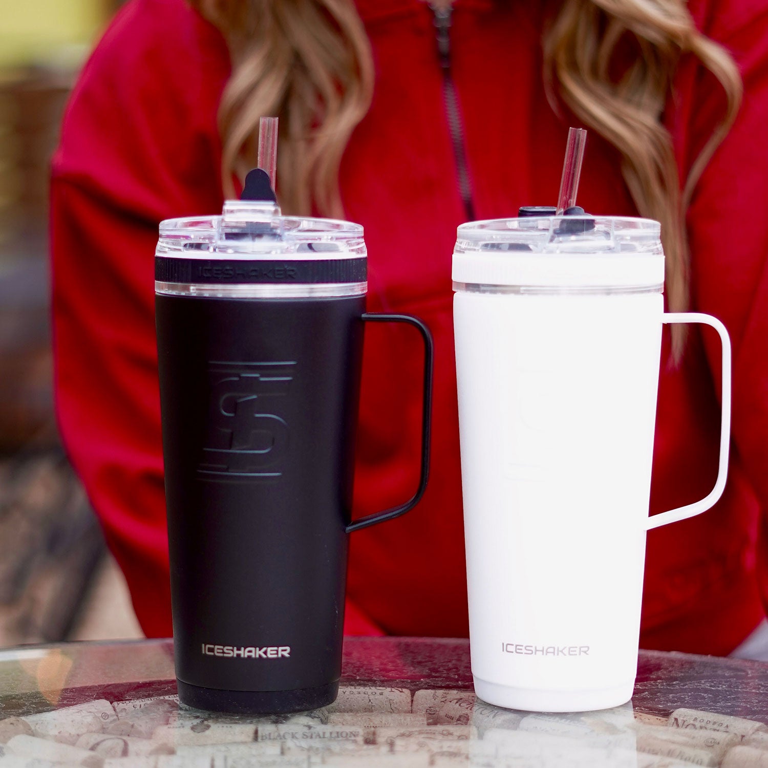 An image of a Black 26oz Flex Bottle and a White 26oz Flex Bottle with a Handle on a table next to each other. A Straw in inserted into both bottles.